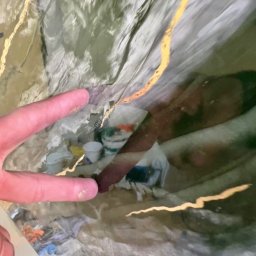 SPONTANDEKOR Tomasz Antoniewicz - Abstrakcyjna faktura ściany z nieregularnymi, złotymi liniami, odbicie osoby i narzędzi malarskich, palec wskazujący na detal. Artystyczne wykończenie wnętrza.