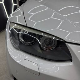 King Art - Biały samochód BMW po detailingu, reflektory i maska z odbiciami lamp w kształcie plastra miodu. Widok z bliska na przód pojazdu, czysty i błyszczący lakier.
