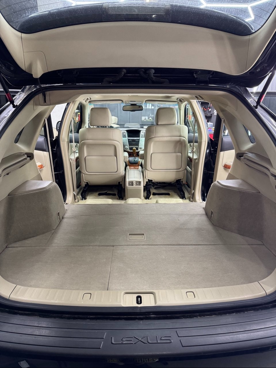 Wnętrze bagażnika Lexus RX z beżową tapicerką po czyszczeniu. Widok z tyłu, otwarte drzwi bagażnika, czyste siedzenia i podłoga. Detal: logo Lexus na zderzaku.