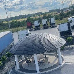 DEKARMAX Jakub Olbryś - Altana z dachem z blachodachówki w nowoczesnym stylu, widok z góry. W tle zaparkowane samochody ciężarowe i słupy wysokiego napięcia.