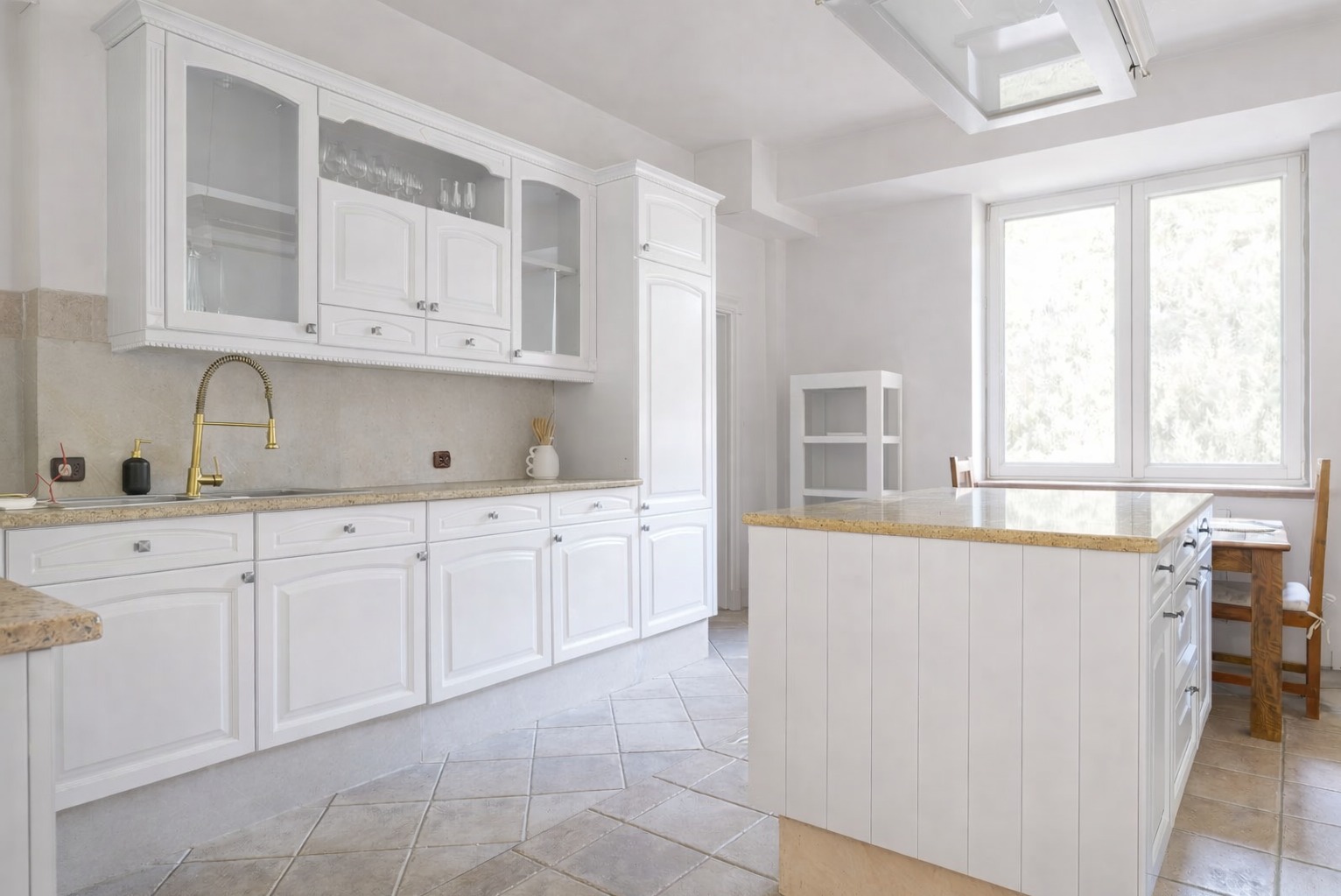 Jasna kuchnia w stylu klasycznym: białe szafki z przeszklonymi witrynami, złota bateria, marmurowy blat i wyspa kuchenna. Uwagę przykuwają płytki podłogowe w romby.