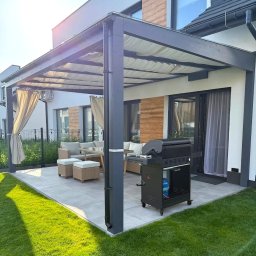 Dtgdrewno - Nowoczesna, szara pergola z zasłonami i szklanym dachem, na tarasie z meblami ogrodowymi i grillem. Widok na zadbany trawnik i dom.