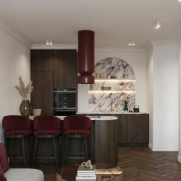 M2 Projekt - Elegancka kuchnia z wyspą i hokerami w odcieniach bordo, marmurowym wykończeniem ściany i nowoczesnym oświetleniem. Parkiet w jodełkę i minimalistyczny design.