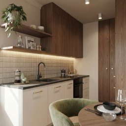 M2 Projekt - Nowoczesna kuchnia z drewnianymi szafkami, beżowymi frontami i podświetlanym backsplashiem z płytek. Okrągły stół z zielonym krzesłem i zastawą.