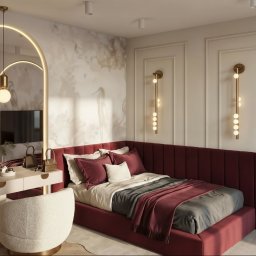 M2 Projekt - Elegancka sypialnia z bordowym łóżkiem i toaletką z lustrem w kształcie łuku. Na ścianie dekoracyjny wzór i złote lampy. Nowoczesny design wnętrza.
