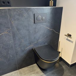 NAKMAR - Nowoczesna toaleta podwieszana w łazience z czarnymi płytkami imitującymi marmur ze złotymi żyłami i złotymi akcentami, widok z dołu.