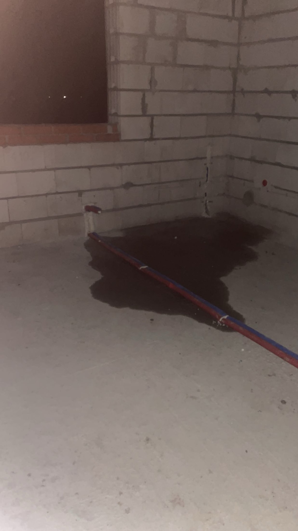 Surowy stan: Instalacja wodna w trakcie prac w pomieszczeniu z surowymi ścianami z betonu komórkowego. Widoczne rury i ślady po wycieku wody na posadzce.