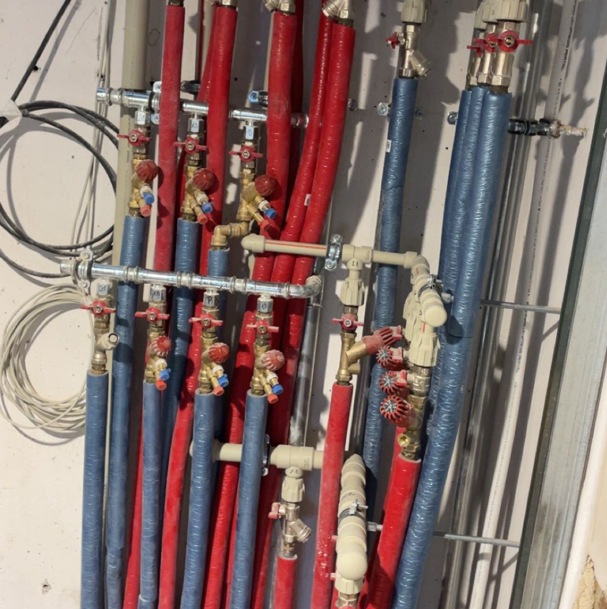 Różnokolorowe, zaizolowane rury instalacji wodnej i grzewczej, prowadzone wzdłuż ściany. Widoczne zawory i złączki. Elementy instalacji zamontowane w nowym budynku.