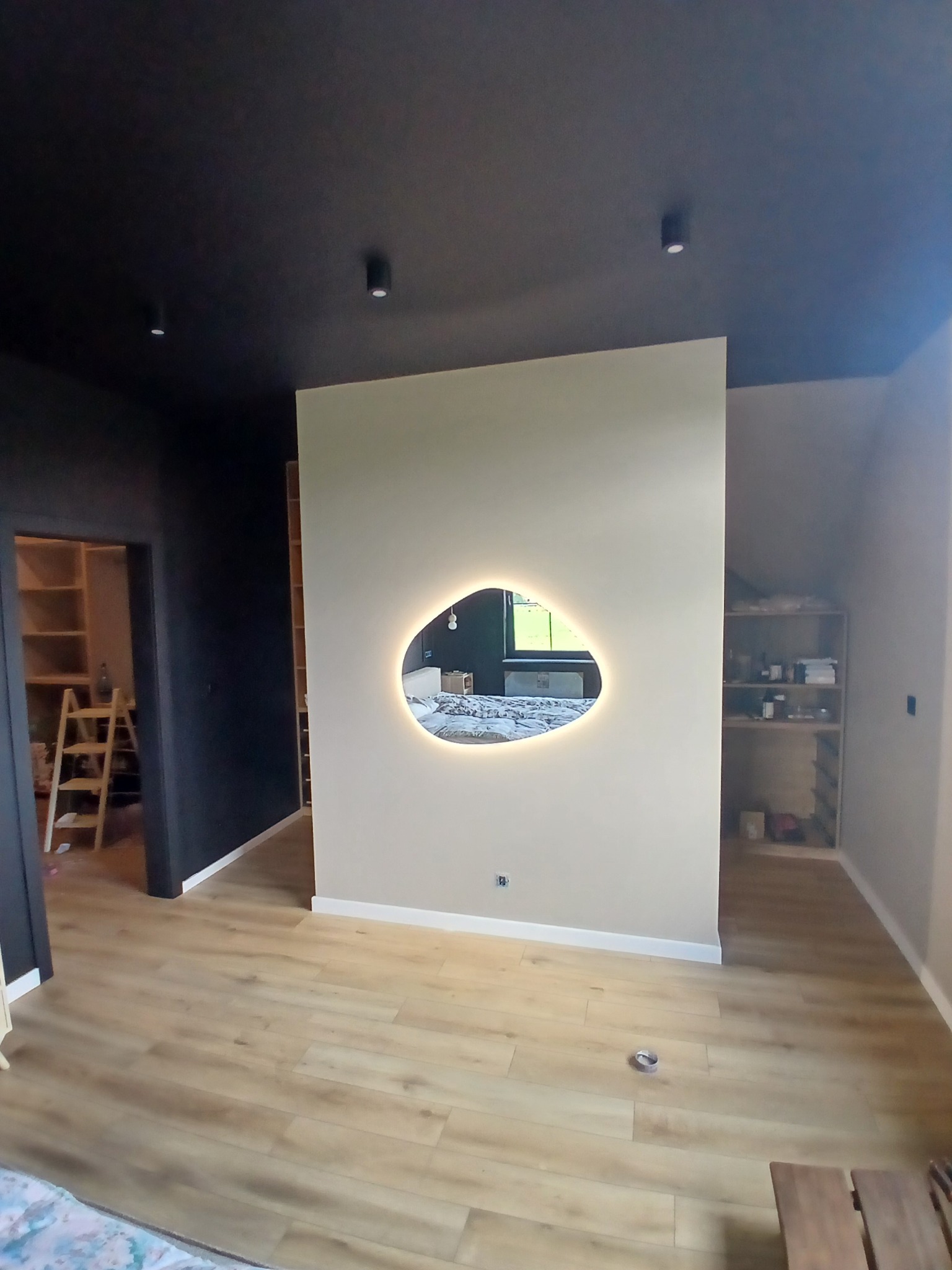 Nowoczesne wykończenie wnętrza: ściana z nieregularnym lustrem z podświetleniem LED, drewniana podłoga, czarny sufit z oświetleniem punktowym. Widok na garderobę.