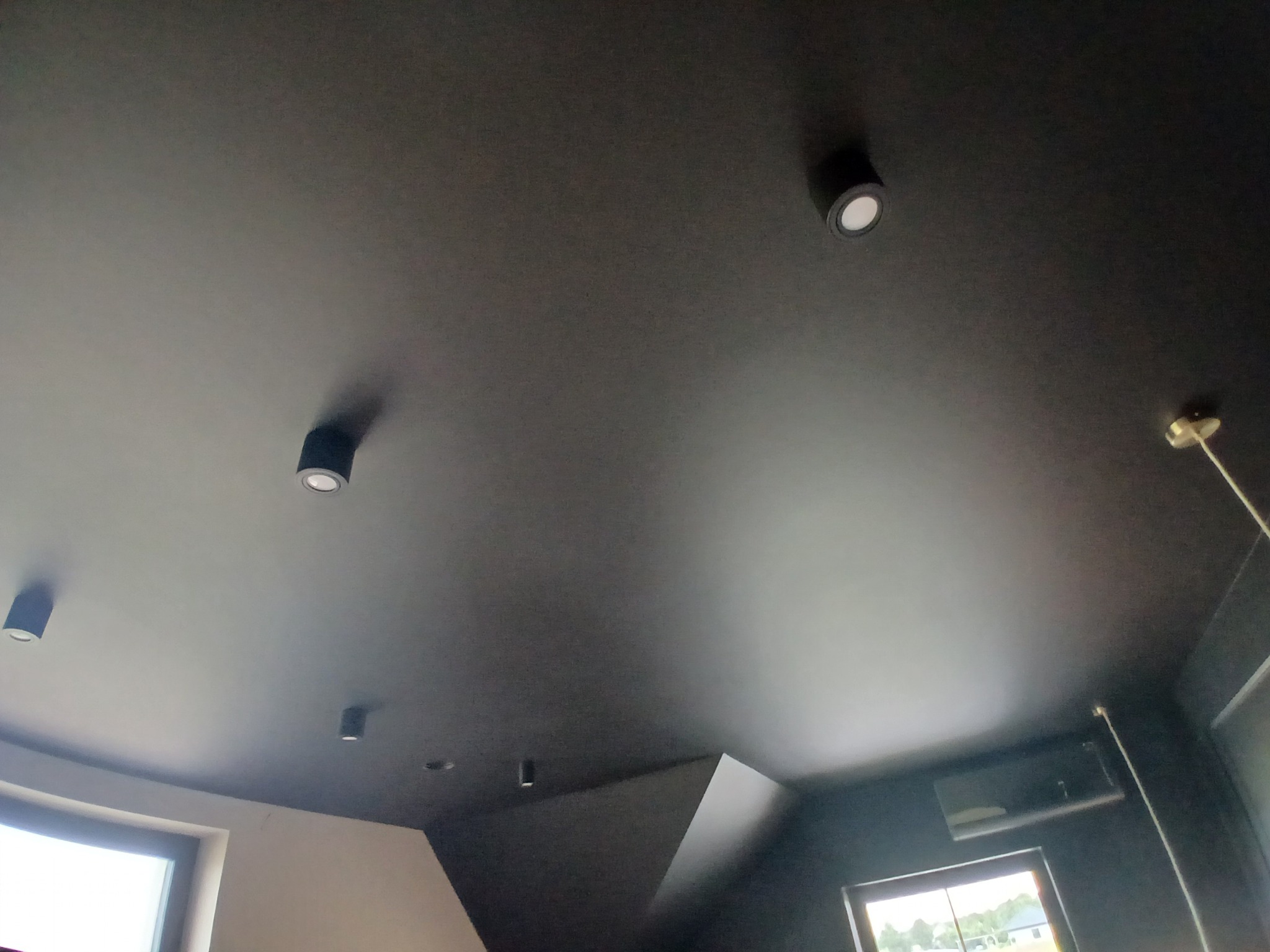 Czarny sufit z punktowym oświetleniem LED, widok z dołu. Minimalistyczny design wnętrza z oknami w tle. Nietypowy kąt ujęcia podkreśla gładką powierzchnię sufitu.