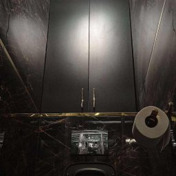 JMBeto - Ciemna łazienka z marmurowymi płytkami, czarną szafką nad toaletą i podświetlanym sufitem. Widok z dołu, ukazujący nowoczesny design i eleganckie wykończenie.
