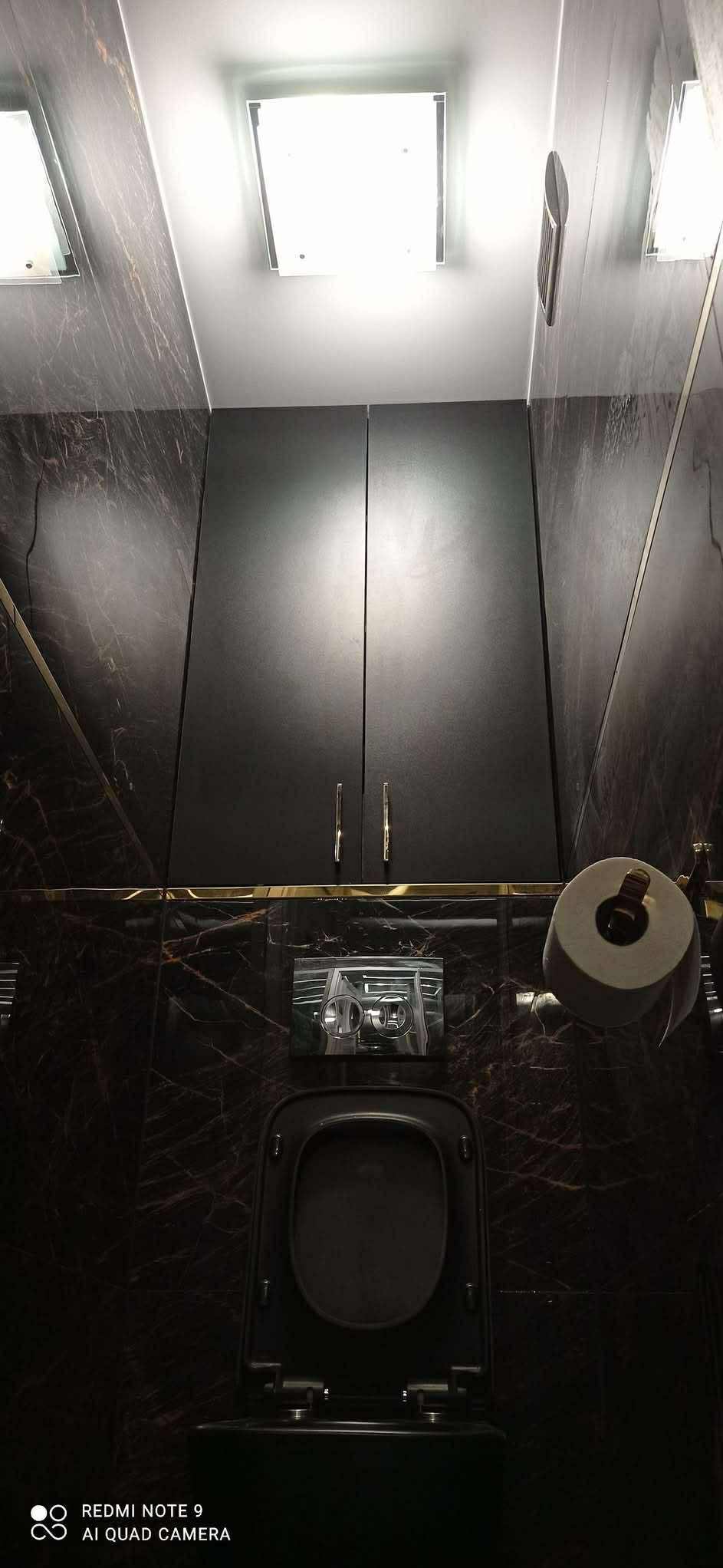 Ciemna łazienka z marmurowymi płytkami, czarną szafką nad toaletą i podświetlanym sufitem. Widok z dołu, ukazujący nowoczesny design i eleganckie wykończenie.