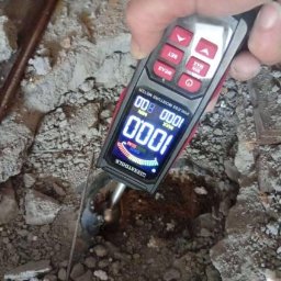 HydroHeros PAWEŁ PRASEK - Pomiar wilgotności podłoża przed wykonaniem ogrzewania podłogowego za pomocą elektronicznego miernika. Widoczne gruz i fragmenty instalacji.