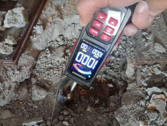 Pomiar wilgotności podłoża przed wykonaniem ogrzewania podłogowego za pomocą elektronicznego miernika. Widoczne gruz i fragmenty instalacji.