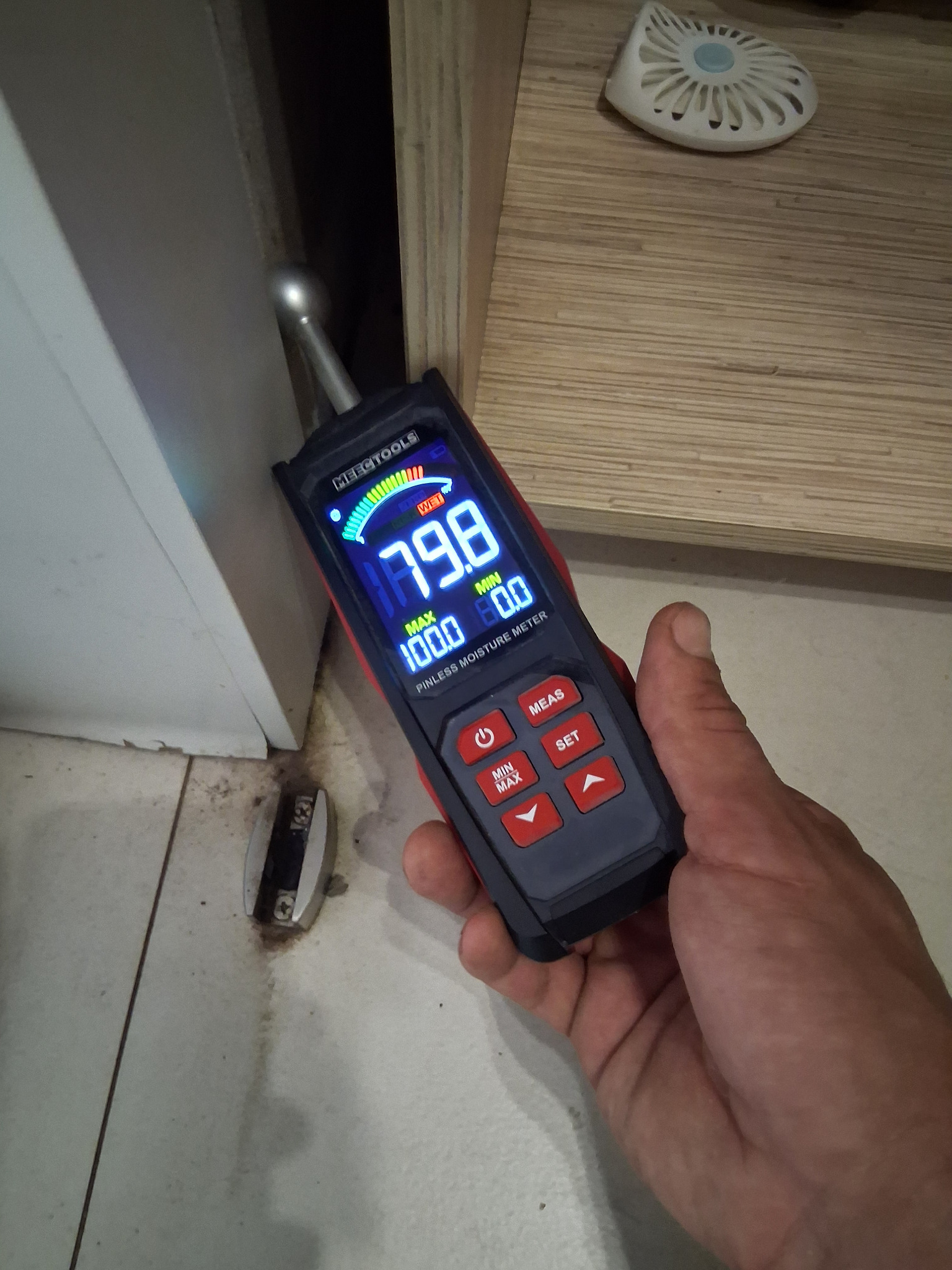 Pomiar wilgotności ściany przy podłodze za pomocą elektronicznego miernika wilgoci. Na wyświetlaczu widoczny wynik 79.8.