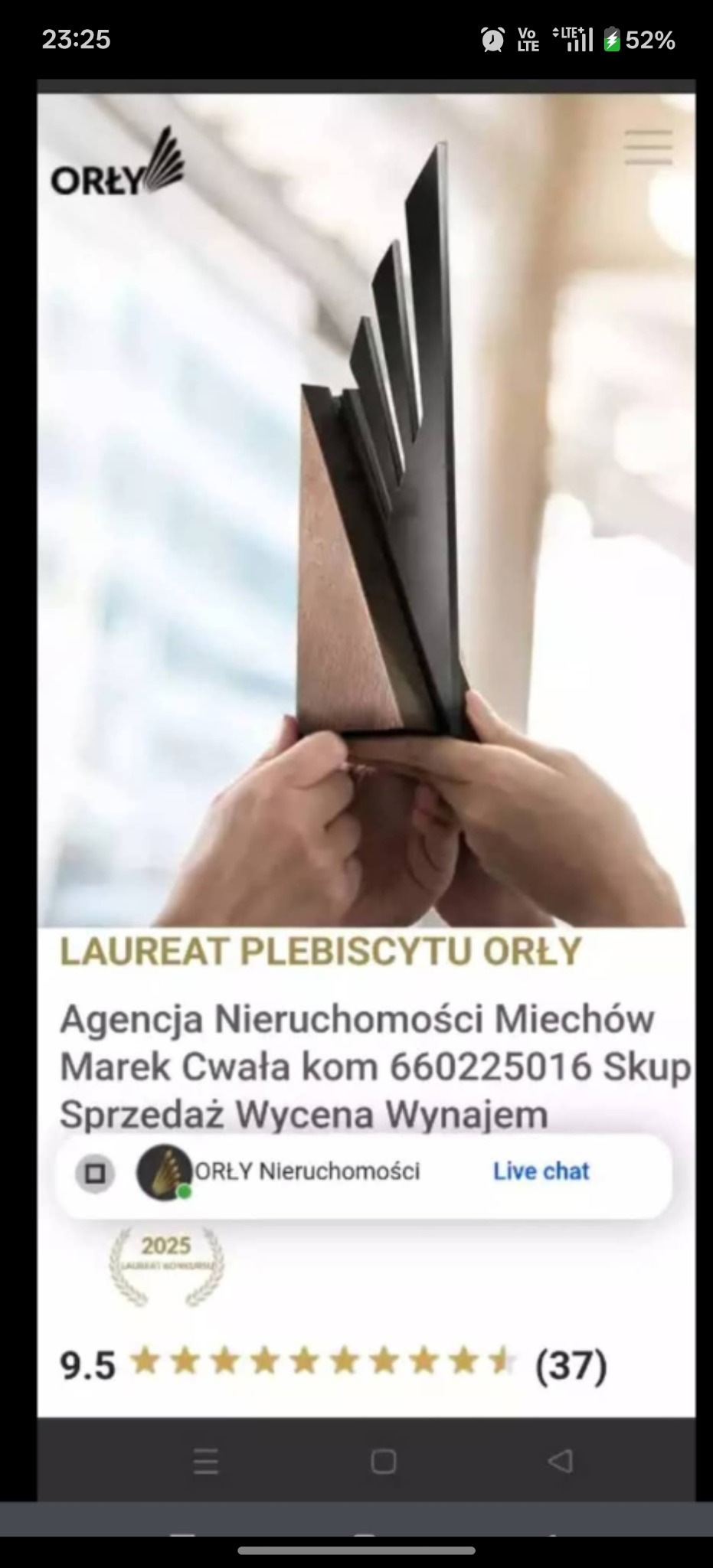Nagroda 'Orły Nieruchomości' trzymana w dłoniach, symbolizująca uznanie dla agencji nieruchomości. Widoczny fragment ekranu telefonu z oceną i nazwą firmy.