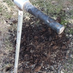 GEOWOL - Wiertnica glebowa wbita w ziemię, obok wykopany otwór. Narzędzie do poboru próbek gleby na trawiastym terenie. Badanie gruntu.