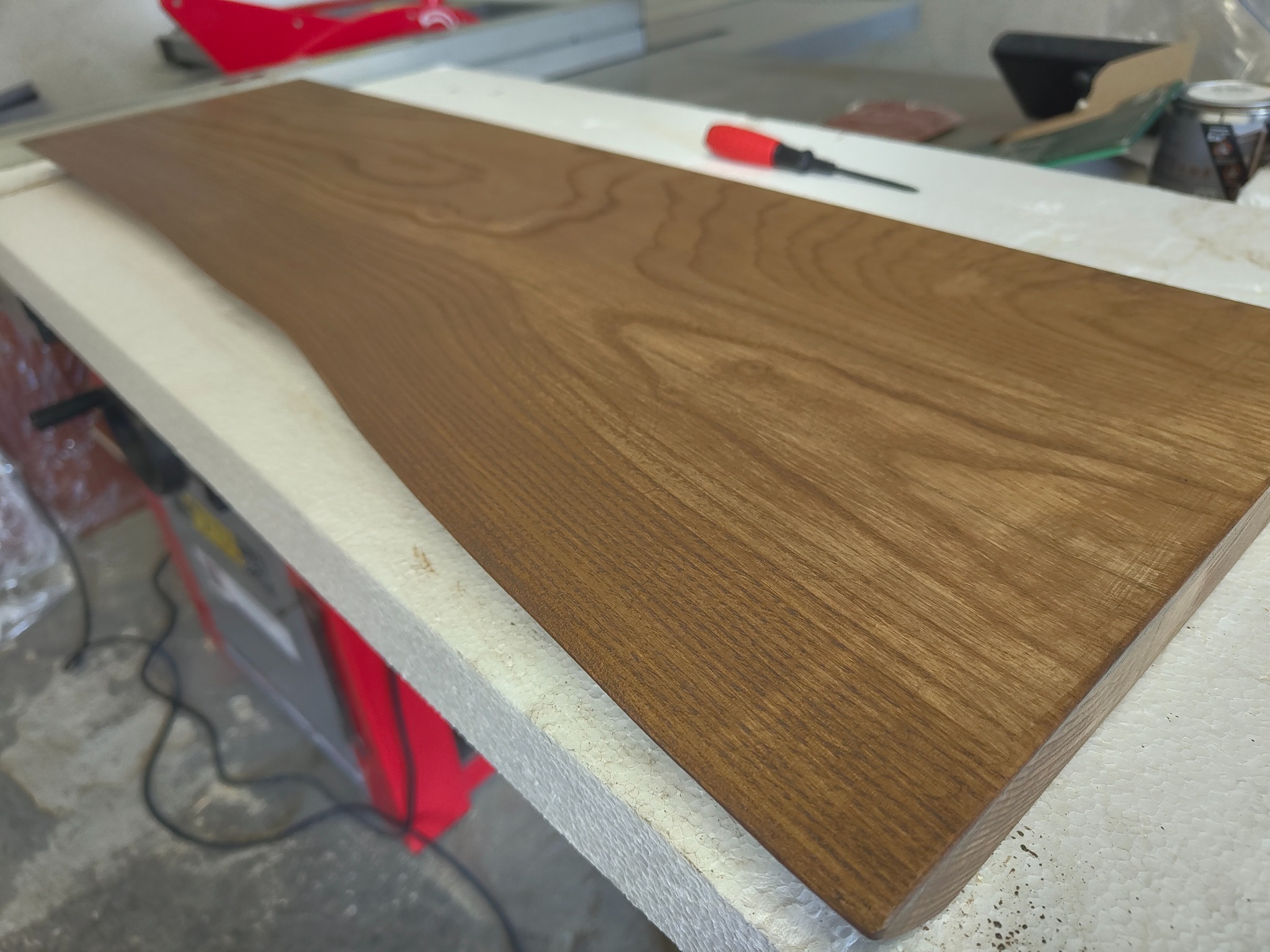 Deska z litego drewna o nieregularnym kształcie, leżąca na białym podłożu w warsztacie w Zduńskiej Woli. Widoczne narzędzia i akcesoria stolarskie w tle.