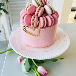 M.S Makaronik - Różowy tort z makaronikami i złotym sercem na białym talerzu, dekorowany tulipanami. Elegancki deser na jasnym tle.