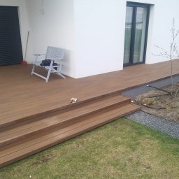 Adam Ziel - Nowoczesny taras kompozytowy z trzema schodkami, szarą ławką i minimalistycznym ogrodem. Widoczne nawodnienie i kamienna obwódka rabaty.