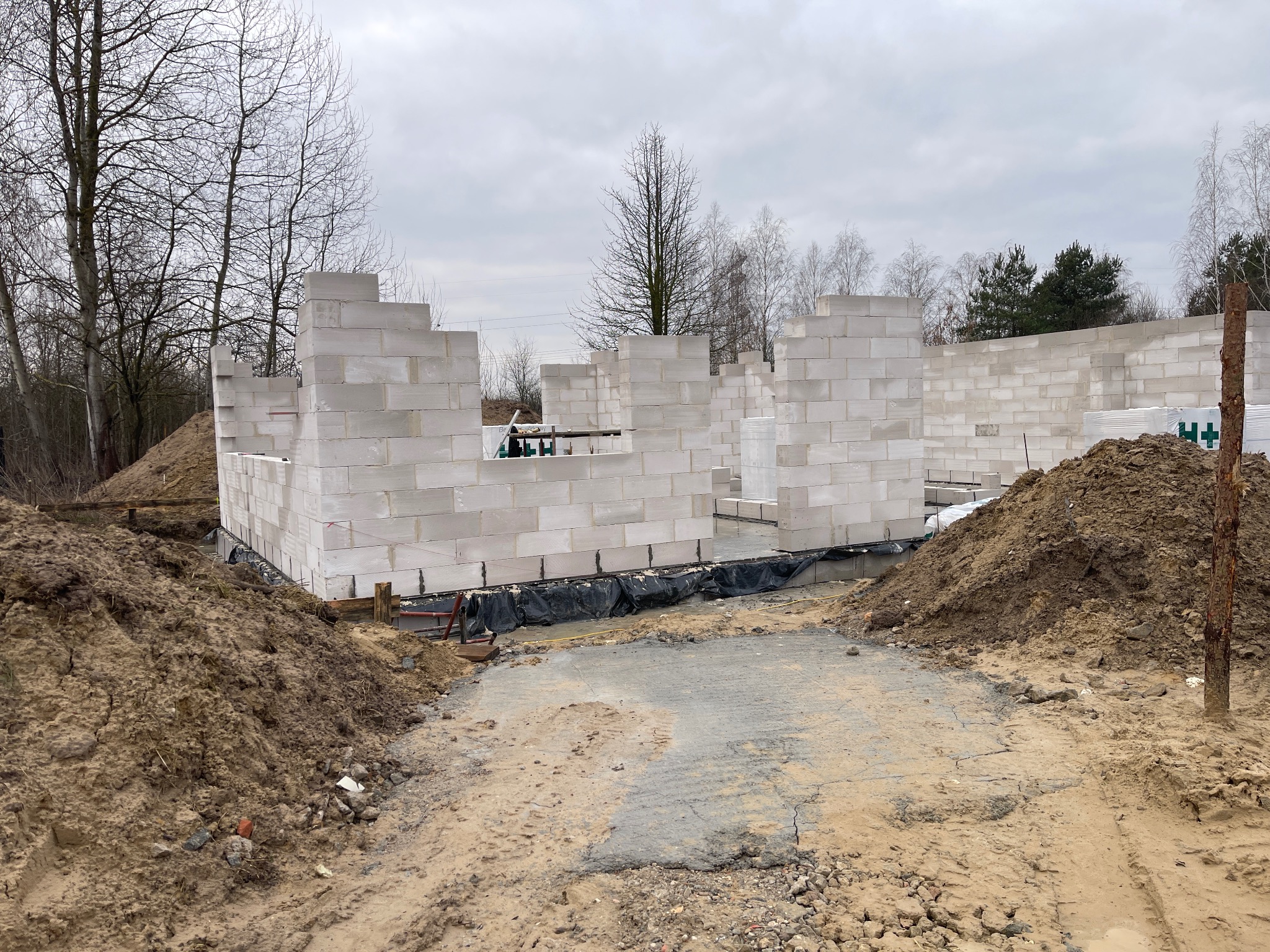 Wznoszenie ścian parteru z bloczków betonu komórkowego Ytong na fundamencie. Budowa domu jednorodzinnego w Warszawie, widok z zewnątrz, pochmurny dzień.