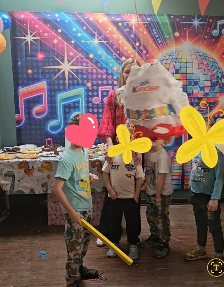 Rozbijanie piniaty Kinder na tle dekoracji z motywem disco. Dzieci czekają na słodycze. Na stole przekąski. Ujęcie z bliska, w pomieszczeniu.