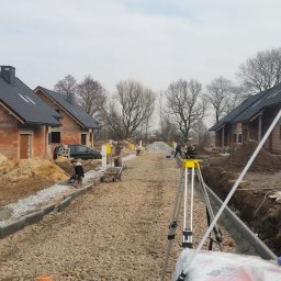 DAN-BUD MOUNTAIN Daniel Jagosz - Budowa osiedla domów jednorodzinnych w trakcie realizacji: widoczne fundamenty, krawężniki, gruz, pracownicy i sprzęt budowlany. Żółta skrzynka gazowa w prawym dolnym rogu.