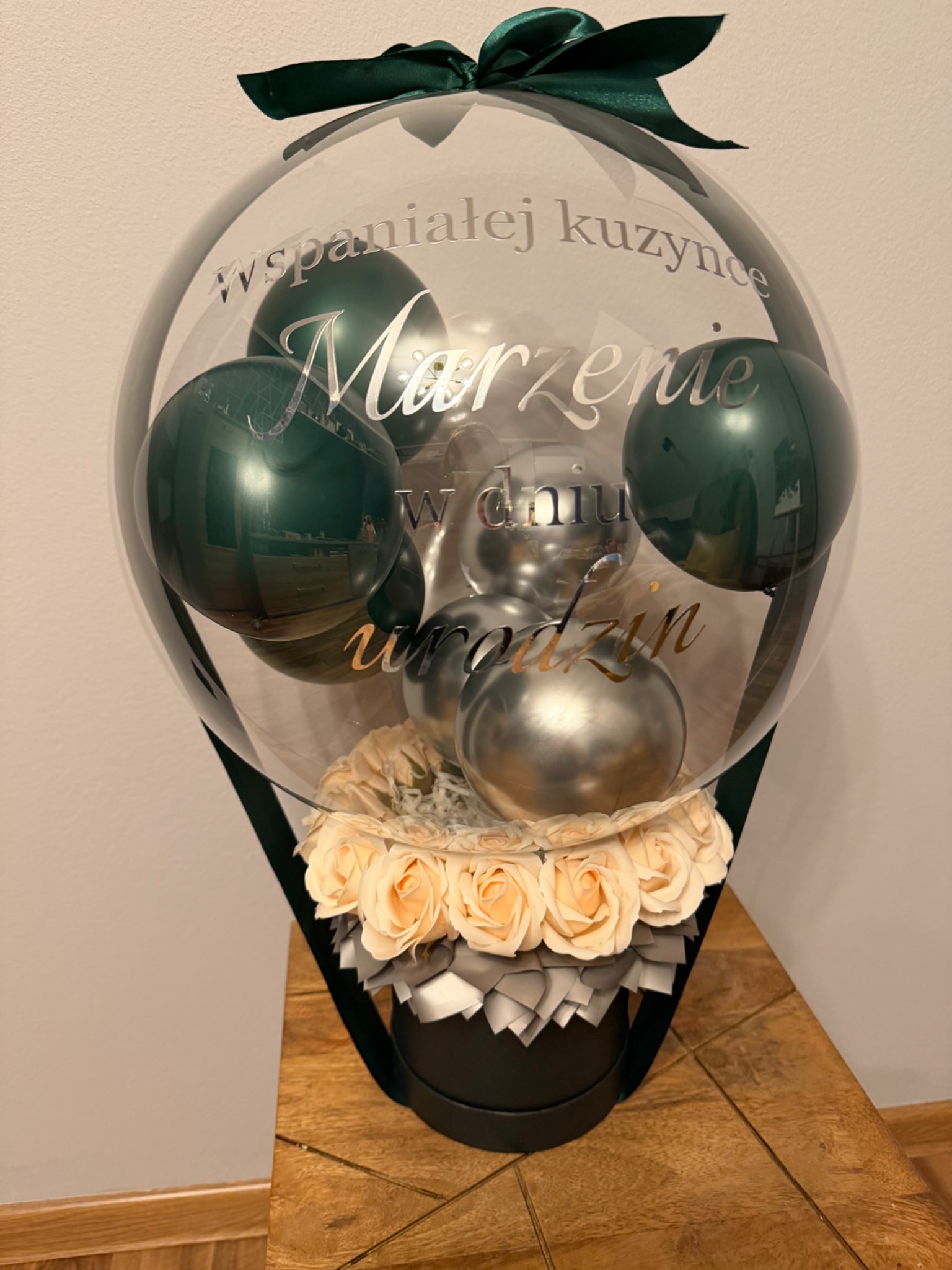 Ozdobny balon z napisem 'Marzenie' i kwiatami w pudełku, przewiązany zieloną wstążką. Idealny prezent na urodziny dla wspaniałej kuzynki.