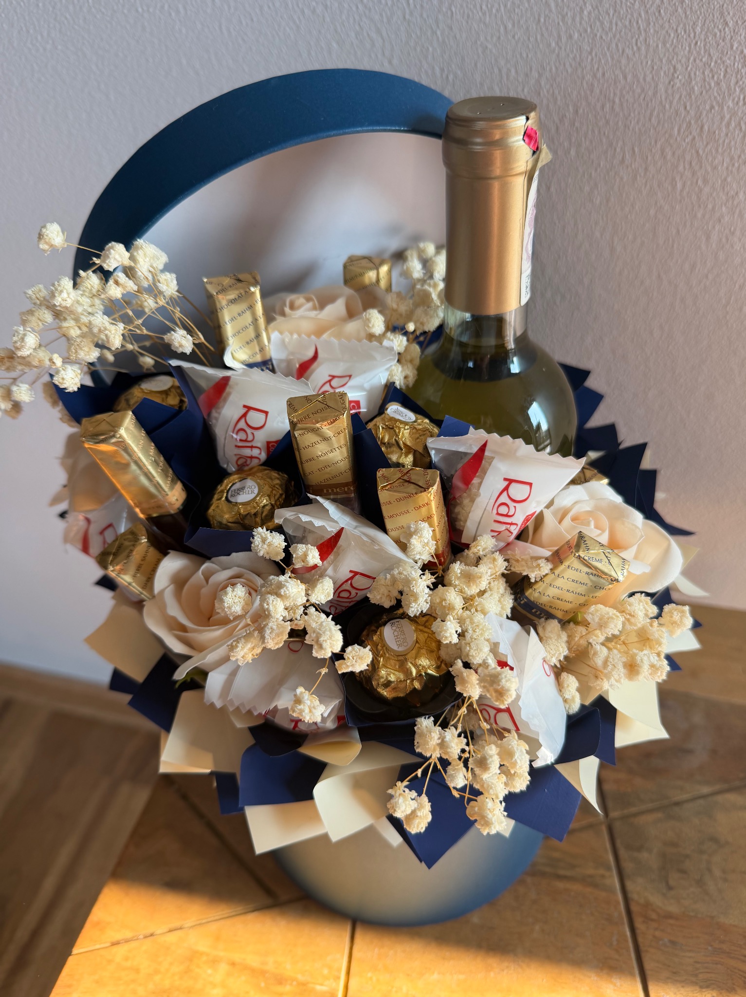 Elegancki kosz prezentowy z winem, kwiatami i słodyczami, udekorowany niebieskimi akcentami, idealny na specjalną okazję. Widok z bliska.