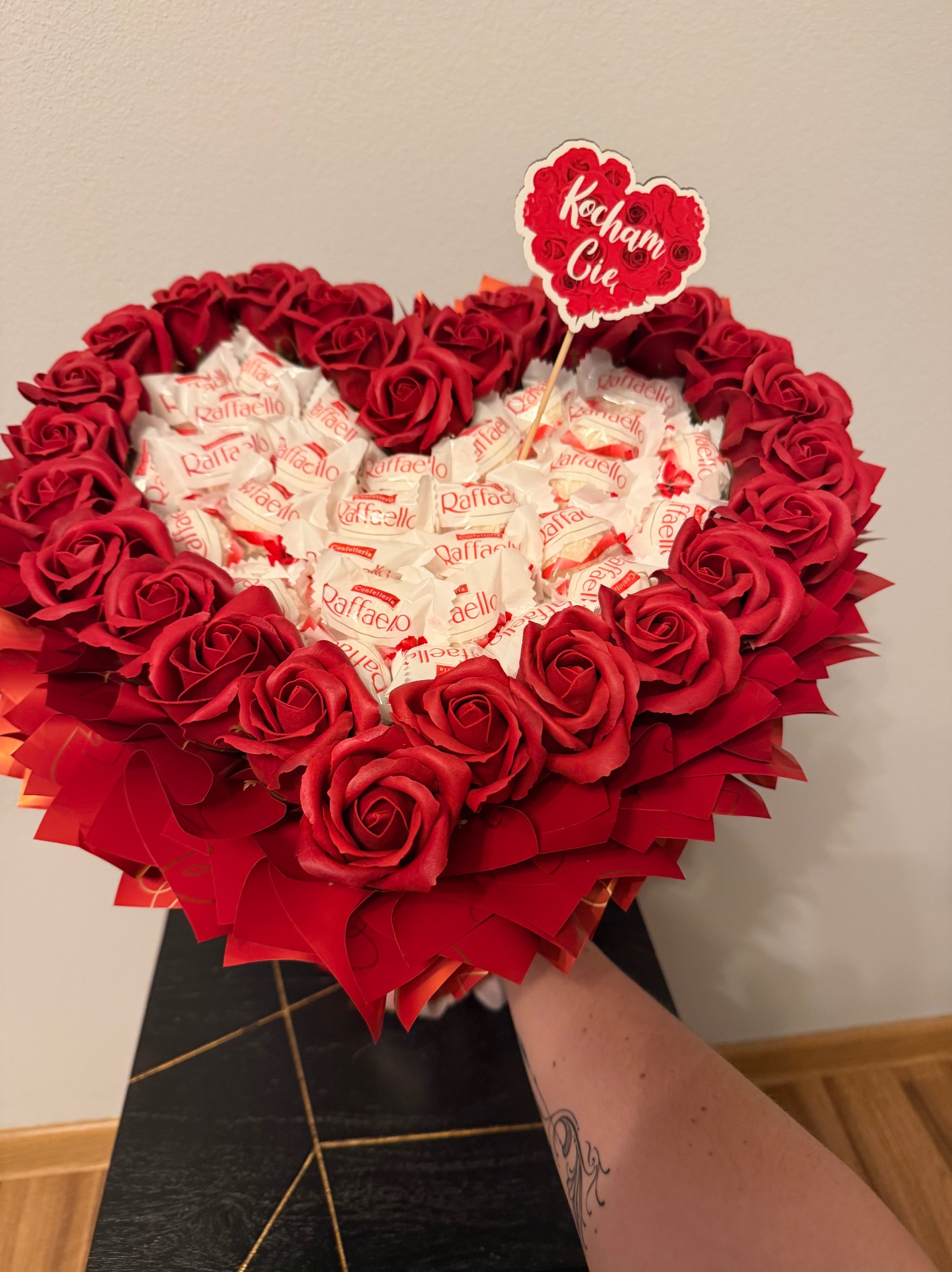 Serce z czerwonych róż i Raffaello, z topperem 'Kocham Cię'. Romantyczny prezent na Walentynki, trzymany w dłoni z tatuażem. Unikalny upominek.