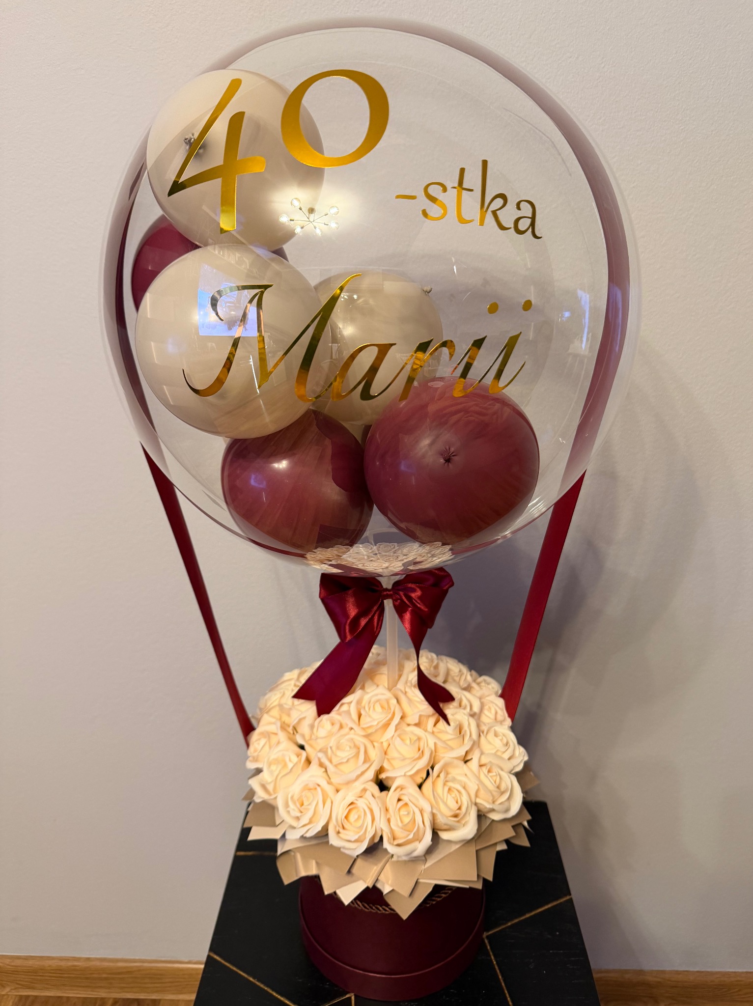 Balon z helem na 40-stkę z napisem 'Marii' i bukietem kremowych róż w bordowym pudełku, przewiązany wstążką. Dekoracja urodzinowa.