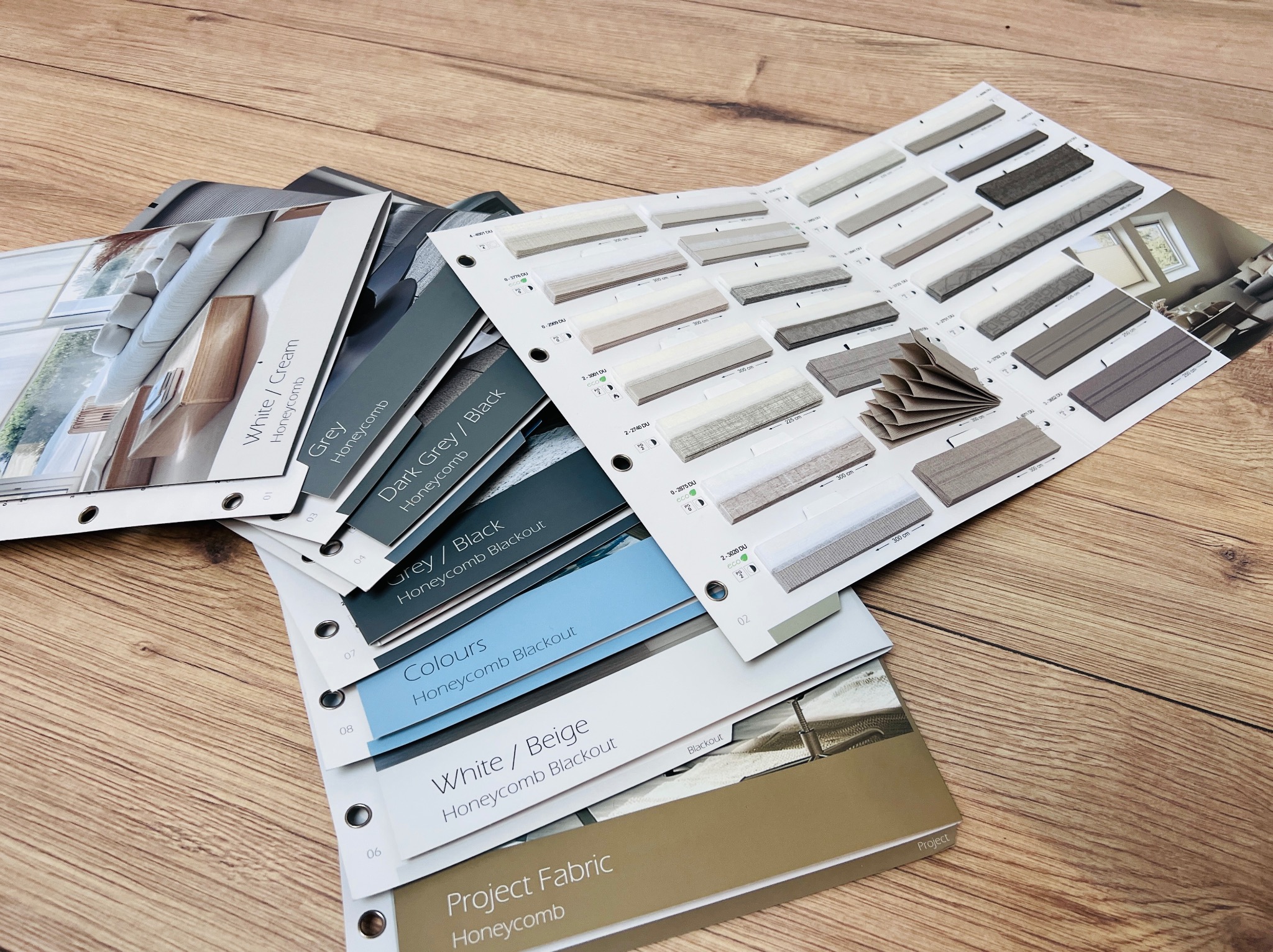 Katalogi z próbkami tkanin do plis honeycomb na drewnianym stole. Widoczne różne kolory i faktury materiałów. Prezentacja oferty.