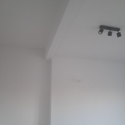 Ihor Serhiiev - Białe ściany i sufit po świeżym malowaniu, widoczna lampa sufitowa z trzema reflektorami. Minimalistyczne wnętrze po remoncie.