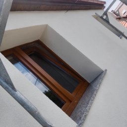 Lewy - Okna z drewnianą ramą i granitowym parapetem w świeżo otynkowanej, białej elewacji budynku. Widoczne rusztowanie. Ujęcie z dołu.