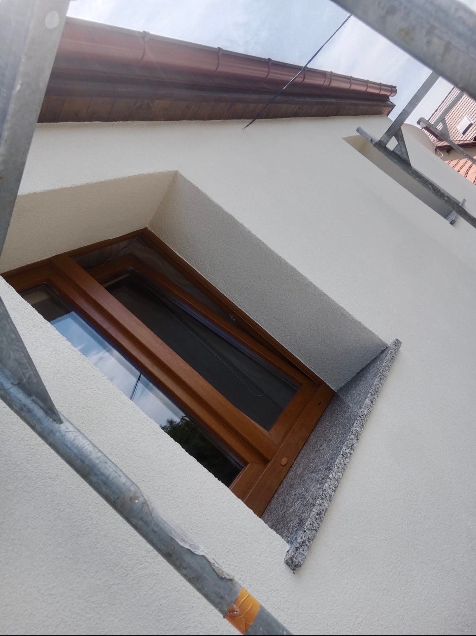Okna z drewnianą ramą i granitowym parapetem w świeżo otynkowanej, białej elewacji budynku. Widoczne rusztowanie. Ujęcie z dołu.