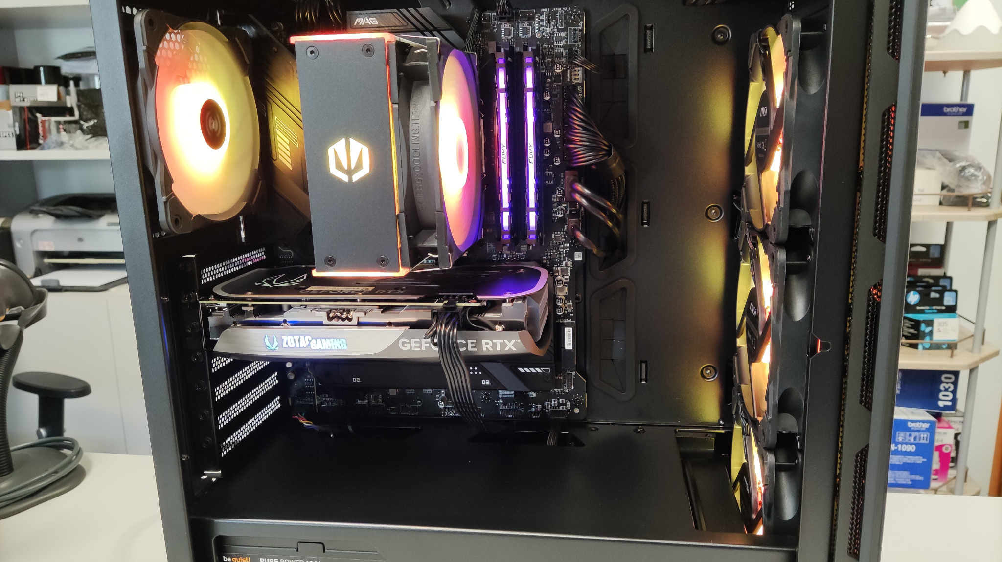 Wnętrze czarnej obudowy komputera stacjonarnego z podświetlanymi wentylatorami, kartą graficzną Zotac i pamięcią RAM Fury. Widoczne chłodzenie procesora MAG.