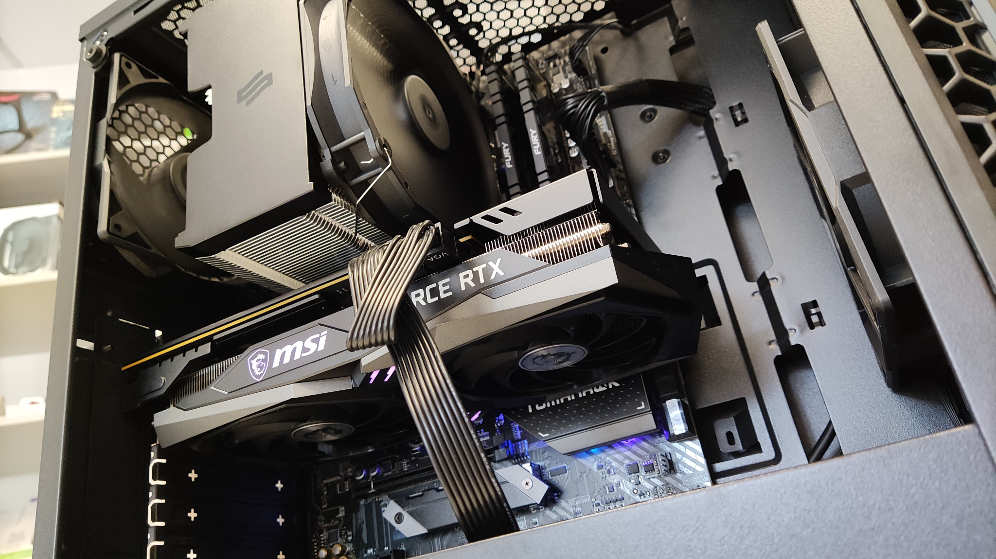 Wnętrze obudowy komputera stacjonarnego z kartą graficzną MSI GeForce RTX, chłodzeniem procesora i pamięcią RAM Fury. Widok z góry, oświetlenie LED.