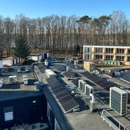 MMS System Sp. z o. o. - Montaż paneli fotowoltaicznych i klimatyzatorów na dachu budynku. Widoczne panele, klimatyzatory, pracownicy podczas instalacji, tło z drzewami i budynkami.