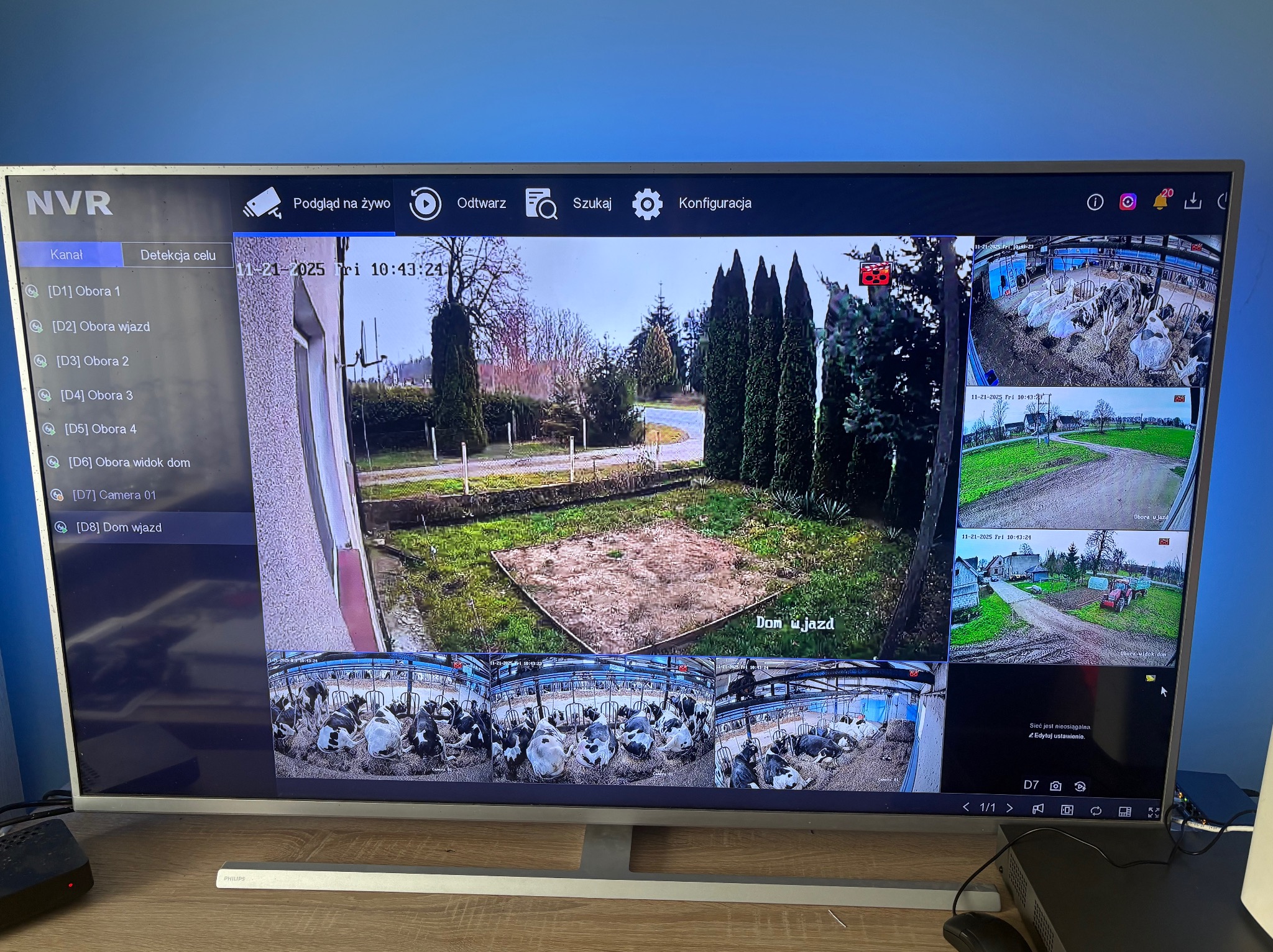 Ekran monitora z podglądem z kamer monitoringu obejmujących obiekty gospodarcze i teren wokół. Widoczne nazwy kamer: Obora 1, Obora wjazd, Dom wjazd.