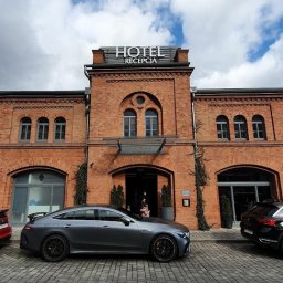Engage Media - Szary Mercedes-AMG GT 63 S E Performance zaparkowany przed ceglanym budynkiem hotelu z napisem 'Hotel Recepcja' w słoneczny dzień.