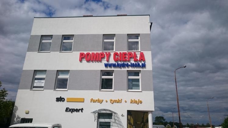 Budynek z reklamą zewnętrzną: czerwony napis 'Pompy Ciepła' nad adresem strony www, poniżej szyld 'STO Expert' i informacja o farbach, tynkach i klejach.