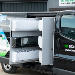 ICE-MAX - Czarny van z otwartymi drzwiami, prezentujący klimatyzatory na półkach wewnątrz. Widoczne logo firmy i numer telefonu na karoserii.