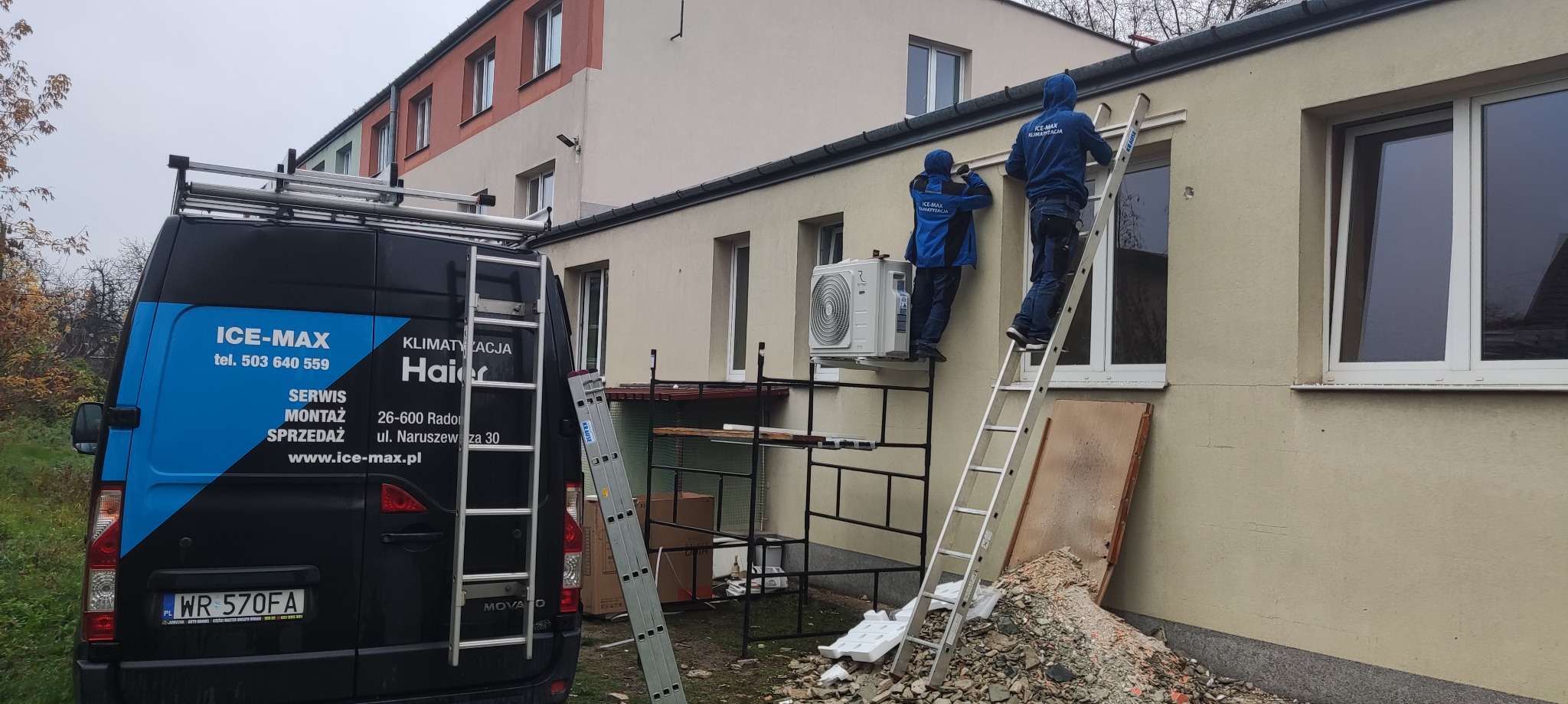 Montaż klimatyzacji zewnętrznej na elewacji budynku przez dwóch monterów w firmowych ubraniach, widoczny firmowy bus z logo Ice-Max i drabiny.