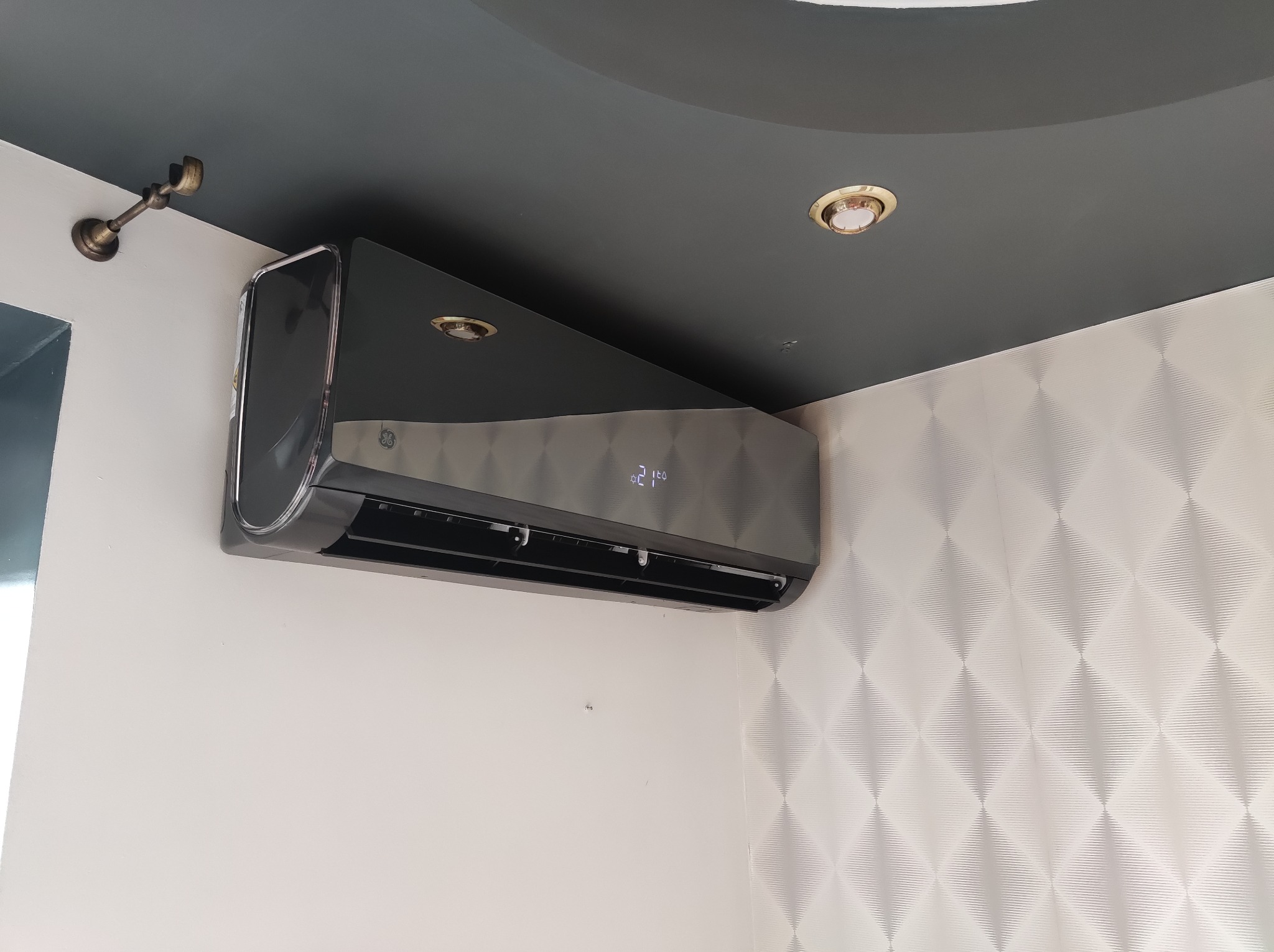 Czarny klimatyzator z wyświetlaczem temperatury zamontowany na ścianie w Radomiu. Nowoczesny design, widoczne oświetlenie sufitowe i dekoracyjna tapeta.