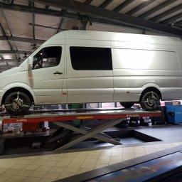 Auto Service Domagała - Niezależny Warsztat Ford - Biały samochód dostawczy na podnośniku w warsztacie. Widoczne narzędzia i wyposażenie warsztatowe. Diagnostyka pojazdu na stanowisku.