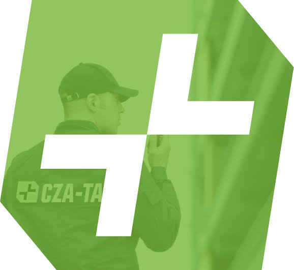 Mężczyzna w zielonym uniformie z napisem 'CZA-TA' i czapce, z krótkofalówką w dłoni, na tle zieleni i białego znaku plus.