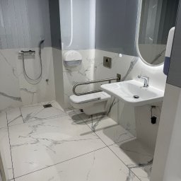 Piotr STARK - Biała, luksusowa łazienka z marmurową podłogą i ścianami. Umywalka, toaleta dla niepełnosprawnych, lustro z podświetleniem. Czystość i minimalizm.