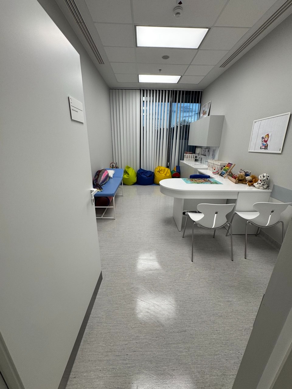 Jasne, minimalistyczne wnętrze poczekalni z kolorowymi pufami, białym biurkiem i krzesłami. Czysta podłoga i ściany. Widok zza rogu, z naciskiem na porządek.