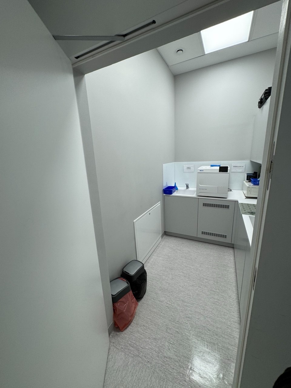 Wnętrze czystego, minimalistycznego pomieszczenia w Ińsku z białymi ścianami, szafkami i podłogą. Widoczne kosze na śmieci i sprzęt laboratoryjny.