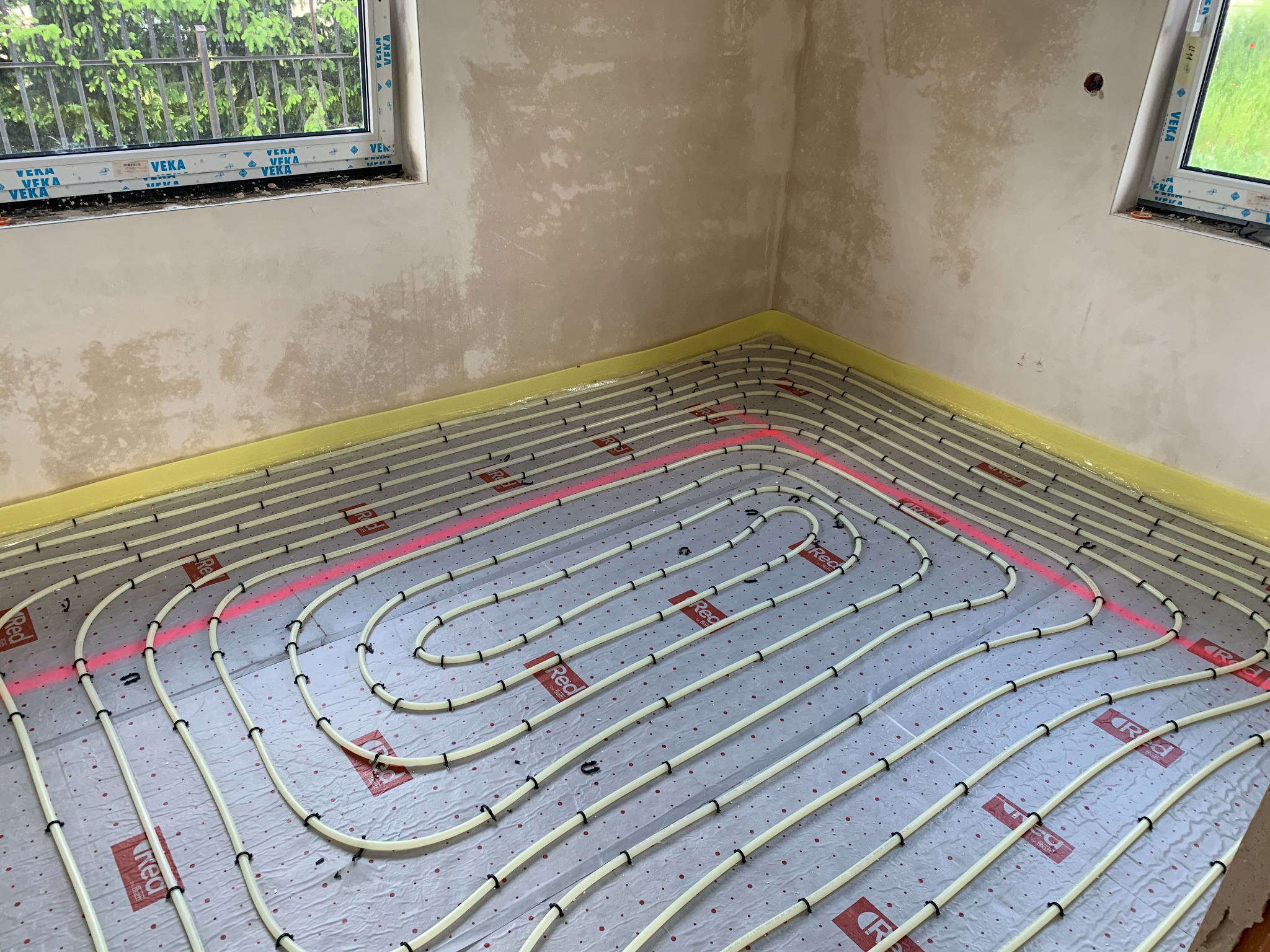 Układanie rur ogrzewania podłogowego na folii z użyciem listew mocujących, widok z góry, w pomieszczeniu w trakcie remontu w Paszowicach.